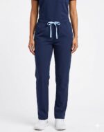 Fundamental para accesibilidad y SEO. Modelo real vistiendo pantalón médico azul marino con pretina elástica y cordón rosa, de corte recto sobre fondo blanco.